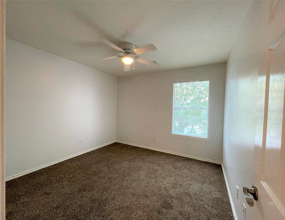 This room features soft carpet flooring, a ceiling fan, and a single window, offering a cozy and bright atmosphere.