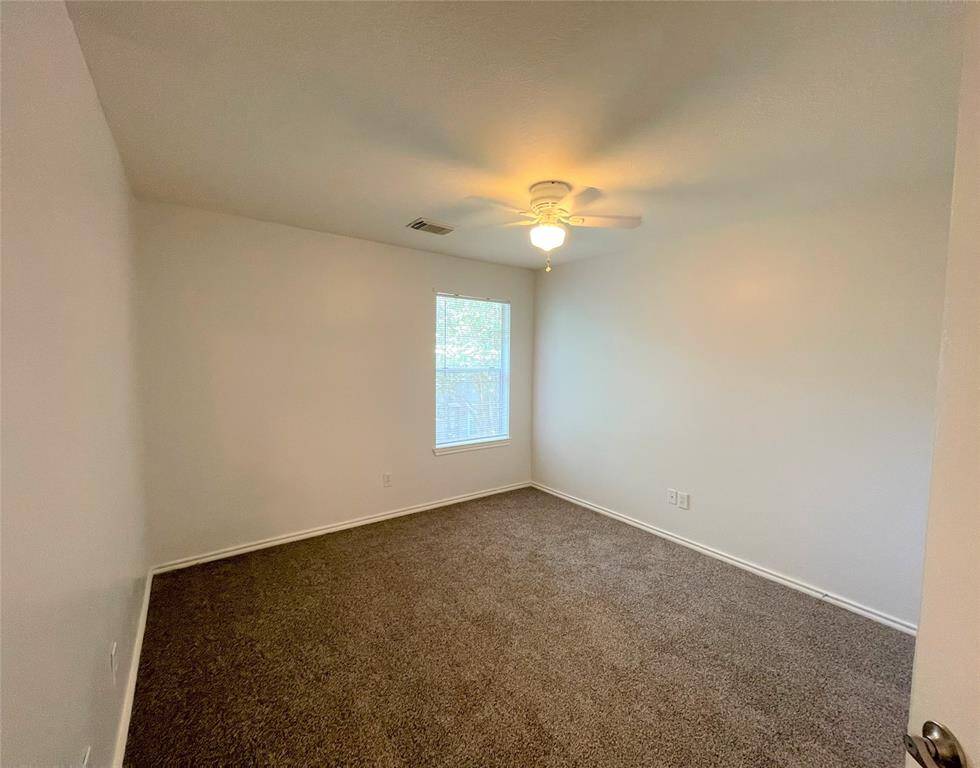This room features neutral walls, a ceiling fan with a light, a window allowing natural light, and cozy carpeted flooring, creating a comfortable space.