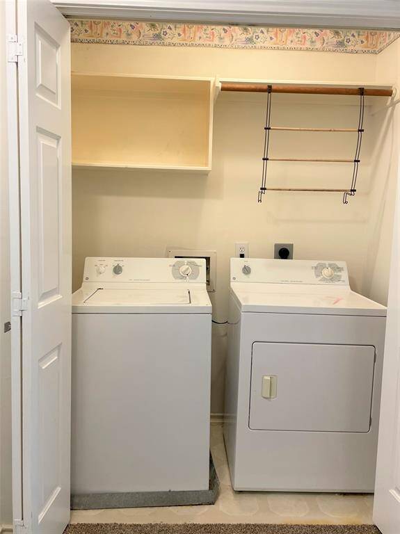 This photo shows a compact laundry area with a top-loading washer and dryer. There's an open shelf and a small hanging rack above the appliances, offering convenient storage and drying space. The area is neatly enclosed with folding doors.