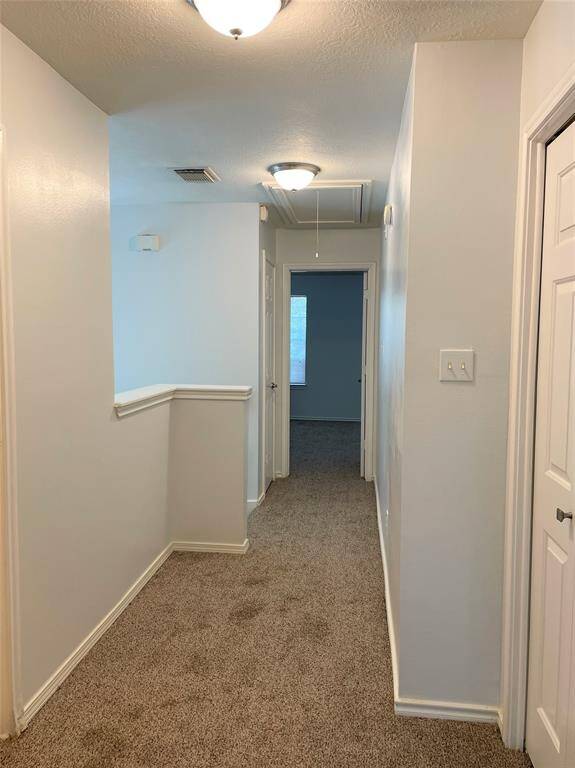 a bright, carpeted hallway with neutral walls and ceiling lights. It leads to a master bedroom at the end, and  2 more bedrooms and a secondary bathroom separated from the master on the long hallway