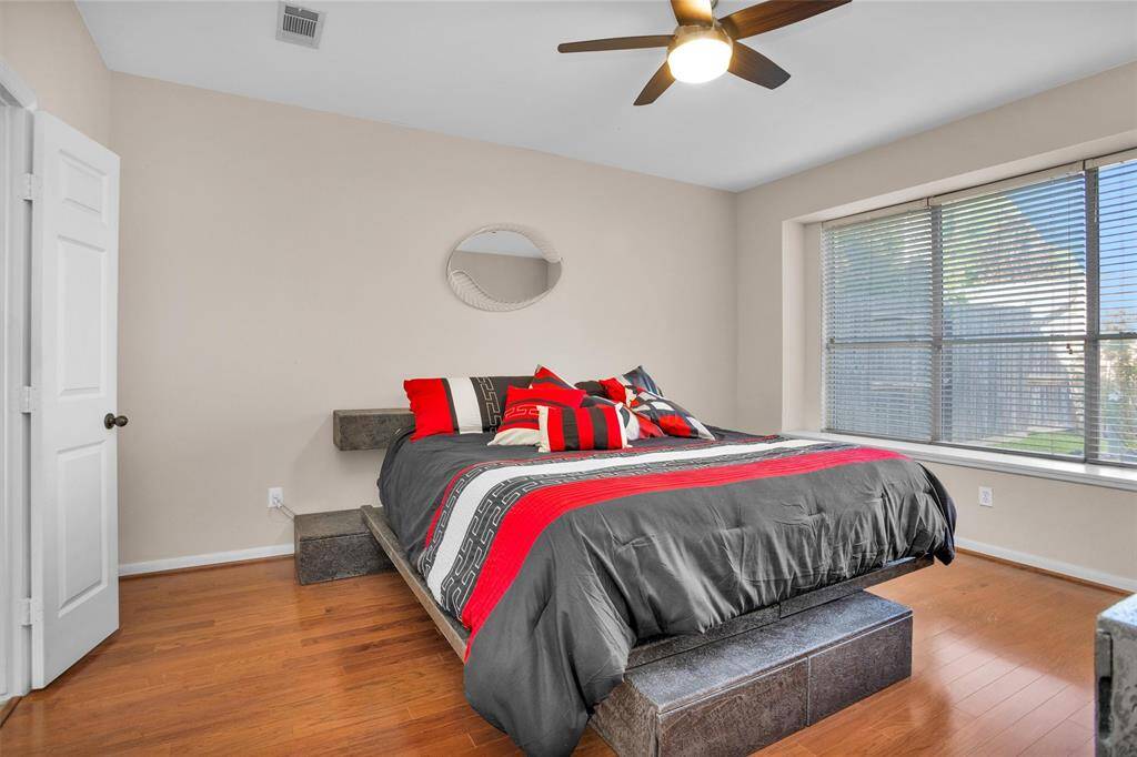 Cozy primary bedroom with hardwood floors, a modern ceiling fan, and large windows providing natural light.