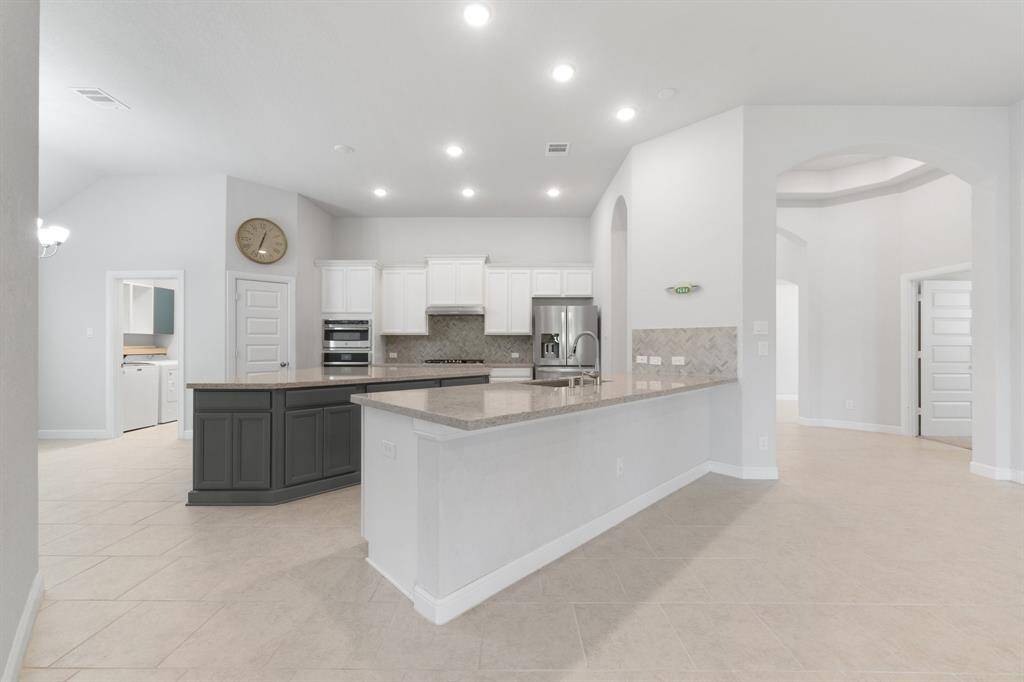 Spacious kitchen with wrap-around countertops, custom backsplash, and a large island—ideal for prepping meals or casual dining. Stylish archways and an open flow connect the space to living and dining areas.