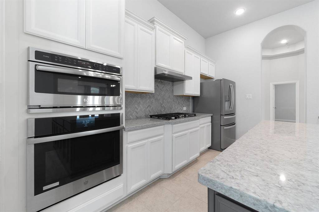 Equipped with double ovens, a gas cooktop, and a vent hood, this kitchen is designed to meet the needs of any home chef. Chevron tile backsplash adds a touch of modern elegance.
