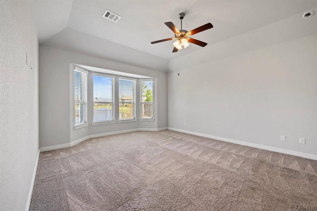 Spacious primary suite with a tray ceiling, plush carpet, and a wall of bay windows showcasing scenic water views.