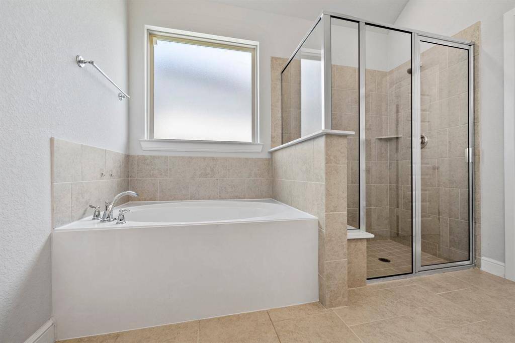 Relax in the oversized soaking tub or step into the glass-enclosed walk-in shower, both surrounded by neutral tile for a spa-like experience.