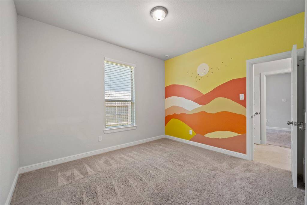 Charming secondary bedroom featuring soft carpet and a bold, custom sunset mural—perfect for a fun and personalized space.