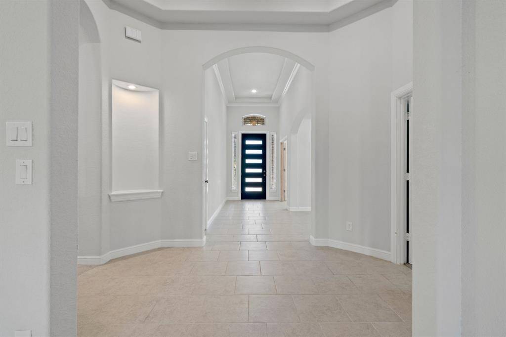 Welcoming entry hall features tray ceilings, decorative niches, and a striking modern front door with frosted glass panels, setting the tone for the rest of the home.
