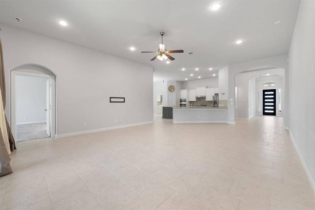 Open-concept living room flows seamlessly into the kitchen and entryway, featuring recessed lighting, a ceiling fan, and arched doorways that add architectural charm.