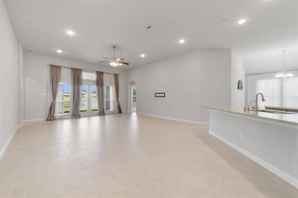 Expansive living area with a wall of windows that flood the space with natural light and offer peaceful views of the water. Neutral tile flooring and high ceilings create a bright, open atmosphere perfect for entertaining.