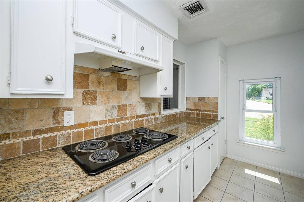 This kitchen features granite countertops, a, and a stylish tile backsplash. White cabinetry provides ample storage, and a window offers natural light.