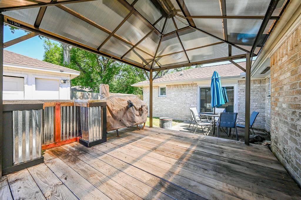 This photo showcases a backyard patio area with a wooden deck and a metal-framed pergola. There is an outdoor seating area with a table and chairs, perfect for entertaining.