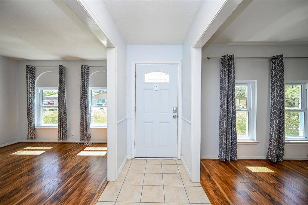 Bright entryway with tile flooring, flanked by rooms featuring large windows, wood flooring.