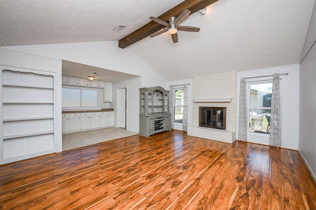 The open layout connects to a bright kitchen with white cabinetry and built-in shelving, perfect for storage and display.