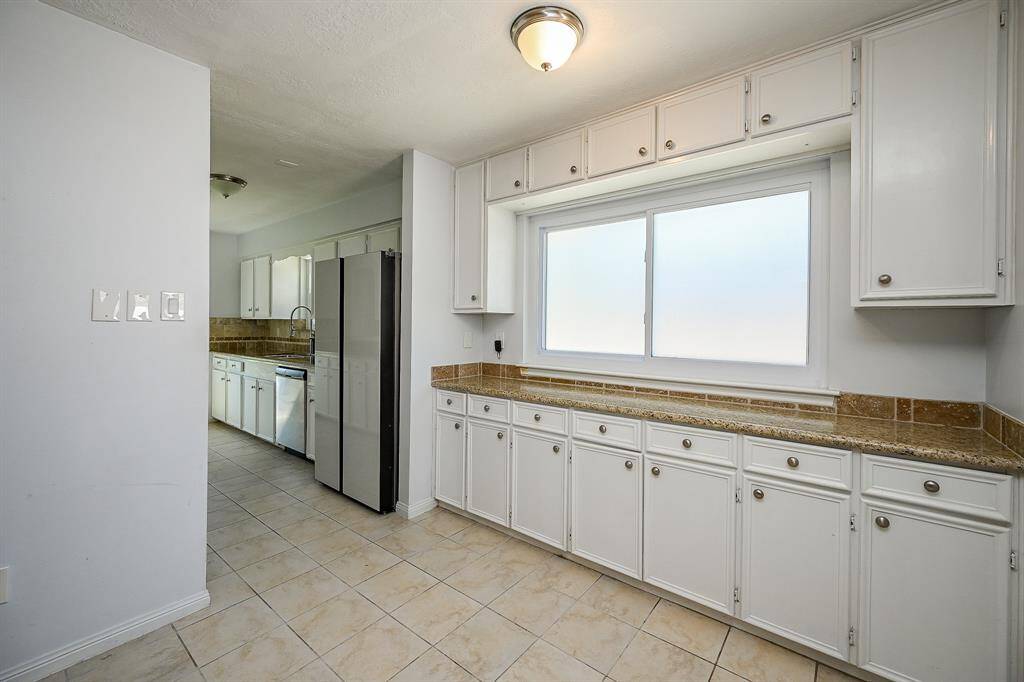 This kitchen features ample natural light, white cabinetry, and granite countertops.
