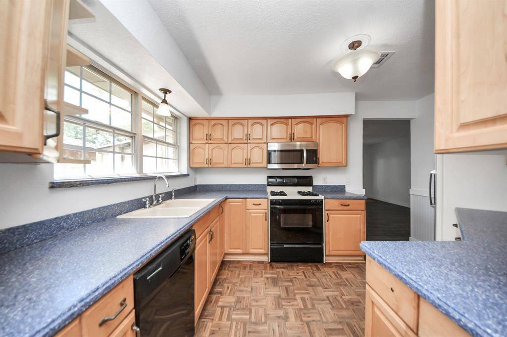 A spacious kitchen equipped with a Whirlpool dishwasher, gas stove, and a stainless steel LG microwave. A large window fills the space with natural light, while abundant cabinets, drawers, and a pantry provide plenty of storage.