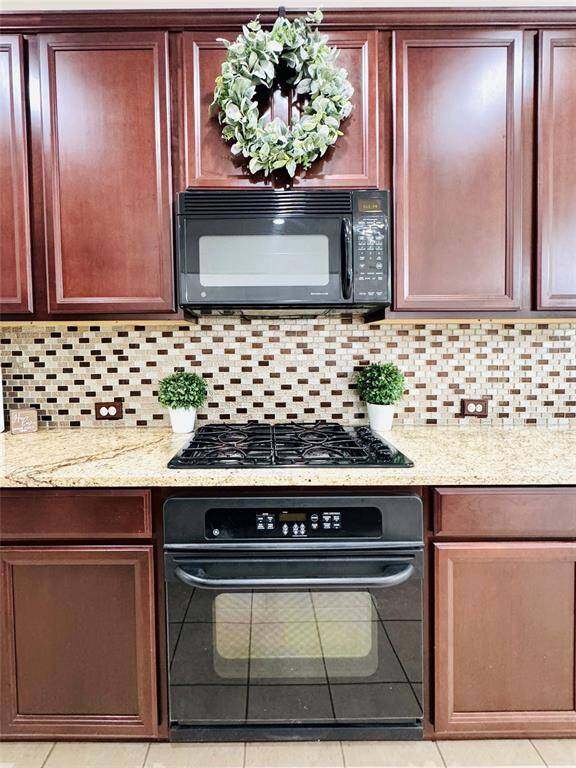 This is a close up of the modern tile backsplash, warm wood cabinetry, a gas cooktop with a built-in oven, and a microwave. This space is perfect for your meal prep and creations!