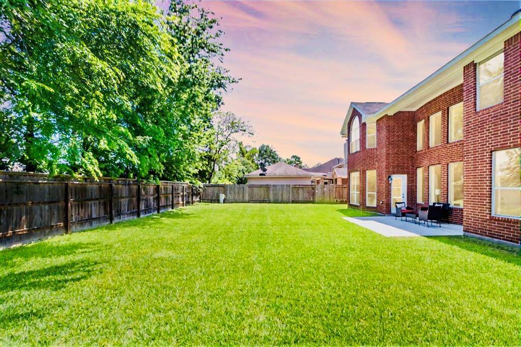 Spacious backyard with lush green lawn, bordered by a wooden fence and mature trees!