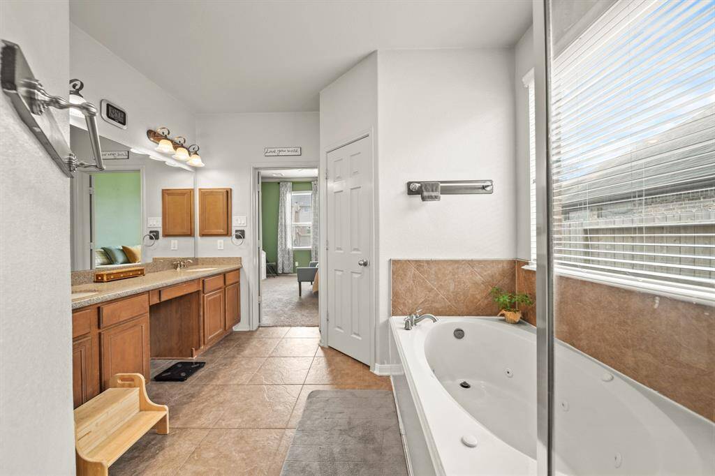 This primary bathroom features separate sinks, a large mirror, granite countertops, vanity area, and beautiful wooden cabinets.