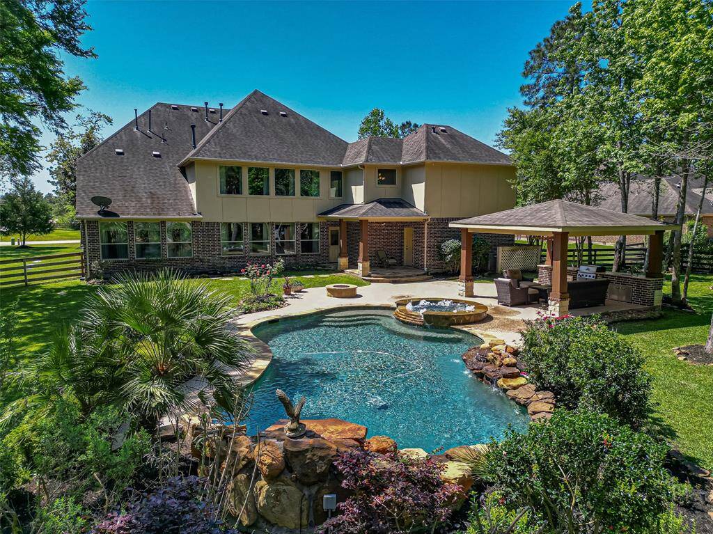 This photo showcases a beautiful two-story home with a spacious backyard featuring a pool, hot tub, and a covered patio area perfect for outdoor entertaining. Surrounded by lush greenery and mature trees, it offers a private and serene setting.