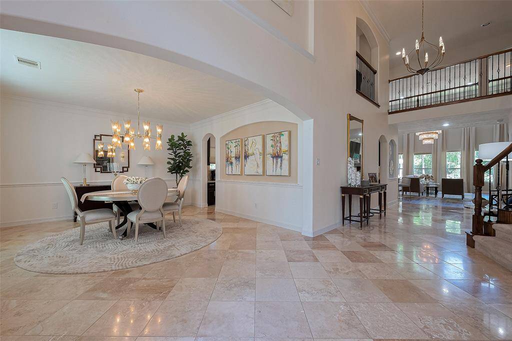 This elegant home features a spacious open floor plan with high ceilings and abundant natural light. The dining area is highlighted by a modern chandelier and polished tile floors. A graceful staircase leads to a second-floor sitting area, overlooking the sophisticated living spaces below.
