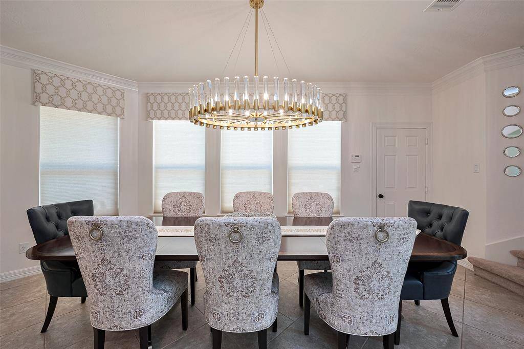 This is a bright, elegant breakfast area featuring a large table with eight upholstered chairs. A newly installed modern chandelier hangs above, and the space is accented with decorative window treatments and subtle wall decor.