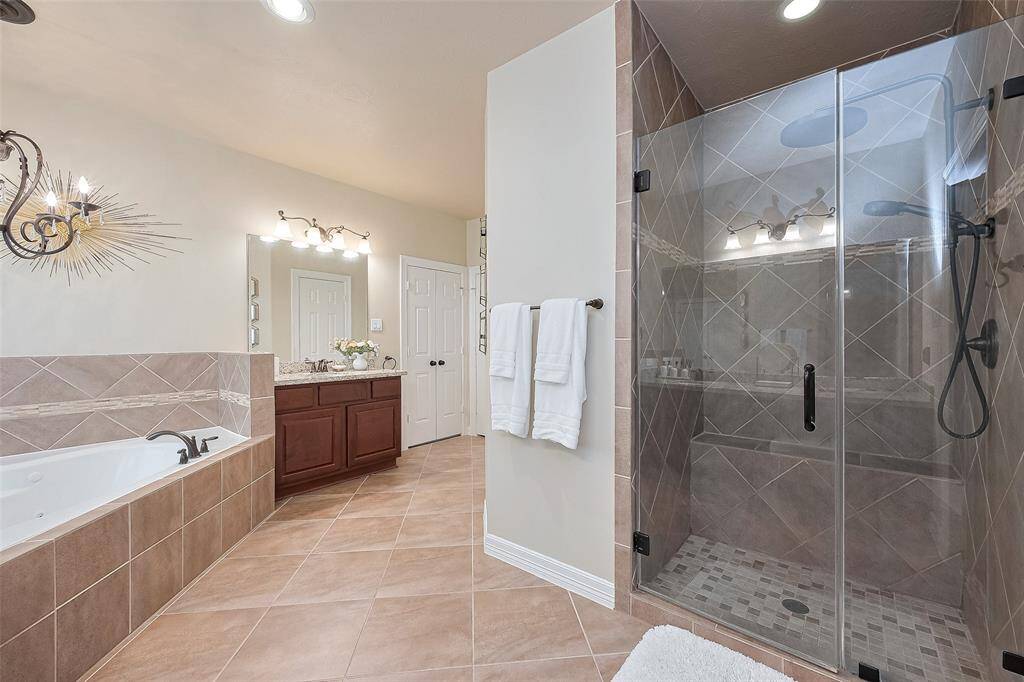 This spacious primary bathroom features a large glass-enclosed shower, a luxurious jetted bathtub, and elegant tile flooring. The dual vanity offers ample storage, enhanced by stylish lighting fixtures and a modern design.
