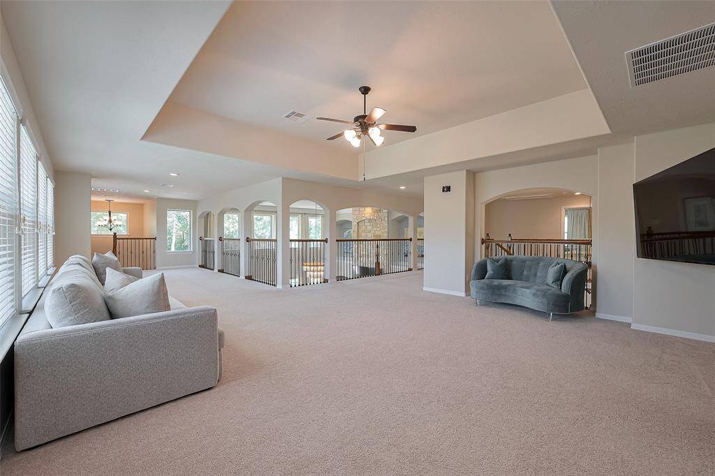 Spacious and bright upstairs living area with neutral carpet, modern ceiling fan, and ample natural light from large windows. Features include a comfortable seating arrangement, open railing overlooking the lower level, and a cozy nook with additional seating. Perfect for relaxation and entertaining.