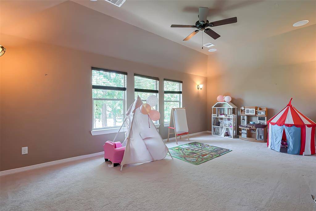 This media room features high ceilings, neutral walls, and ample natural light from large windows. It's currently set up as a playroom, with a play tent, dollhouse, and drawing easel, providing a versatile space for family activities.
