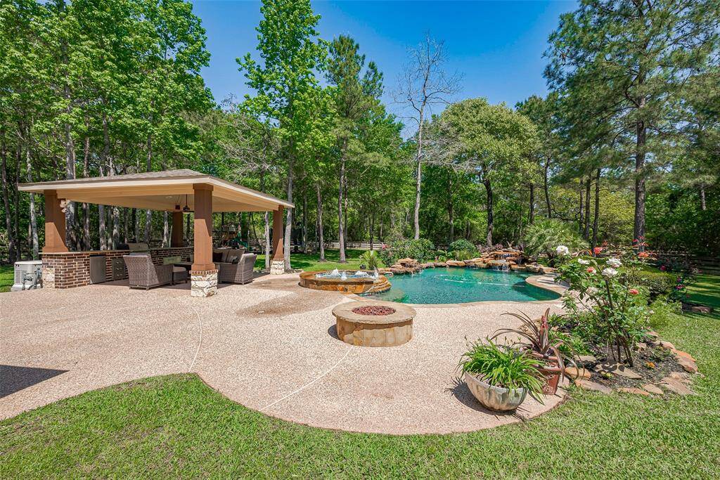 This backyard features a spacious patio with a covered seating area, lush greenery, and a serene pool with a rock waterfall. Ideal for relaxation and entertaining, the space is complemented by a built-in fire pit and vibrant landscaping.