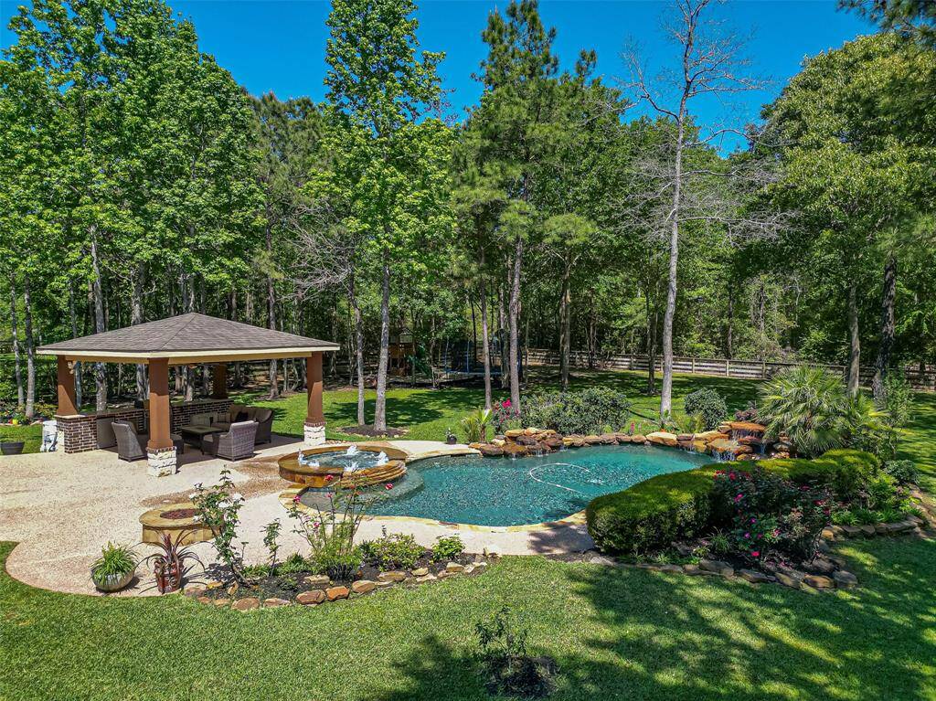 This backyard oasis features a beautiful pool with a rock waterfall, surrounded by lush greenery and mature trees. A spacious covered patio offers ample seating and a cozy outdoor living space, perfect for relaxation or entertaining.