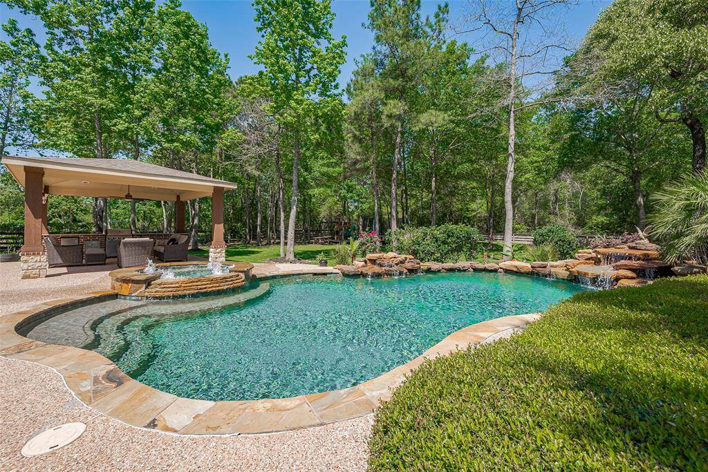 This photo showcases a serene backyard oasis with a sparkling pool, a hot tub, and a covered patio area. The lush greenery and surrounding trees offer privacy and a natural ambiance, perfect for relaxation and entertaining.