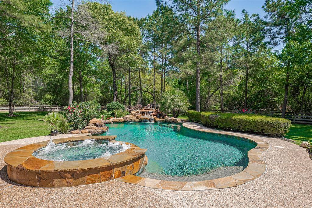 This photo showcases a beautiful backyard with a sparkling pool and spa, surrounded by lush greenery and trees, offering a serene and private retreat.