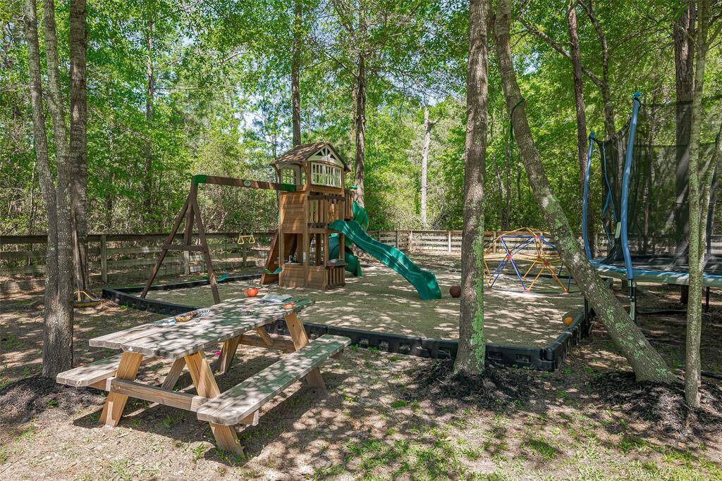 This backyard features a charming playground area with a wooden playset, slide, swing, and climbing dome, all surrounded by trees for shade. A picnic table offers a perfect spot for outdoor gatherings.