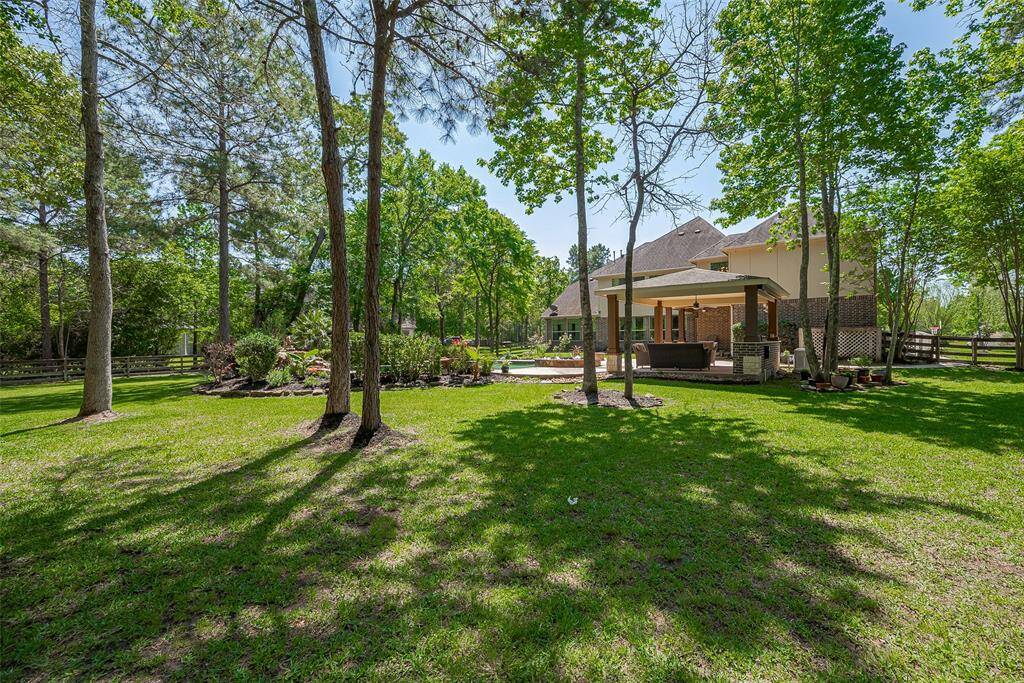 This photo showcases a spacious backyard with lush green grass and mature trees, offering a serene and private setting. The home features a covered patio area, ideal for outdoor entertaining. The surrounding landscape provides a natural, tranquil atmosphere.