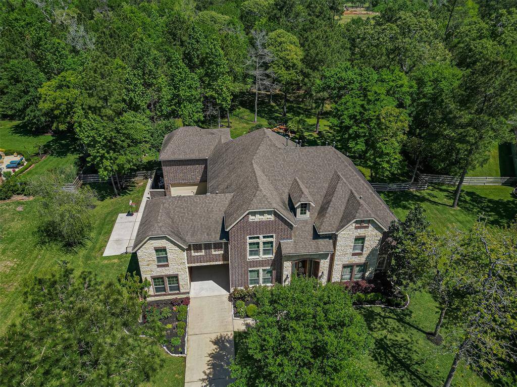 This aerial view showcases a spacious two-story brick home surrounded by lush greenery. The property features a long driveway, well-maintained landscaping, and ample wooded privacy, ideal for a serene living environment.