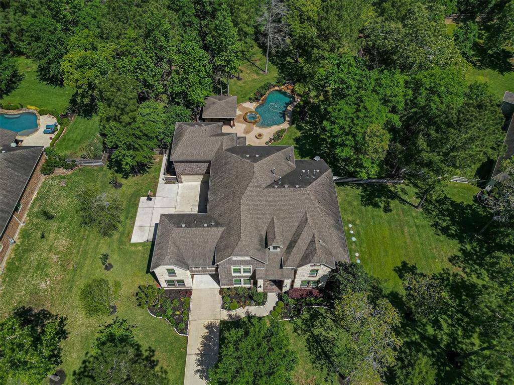 This aerial view showcases a spacious, elegant home with a large, landscaped yard and a beautiful pool, surrounded by lush greenery, offering privacy and a serene environment.