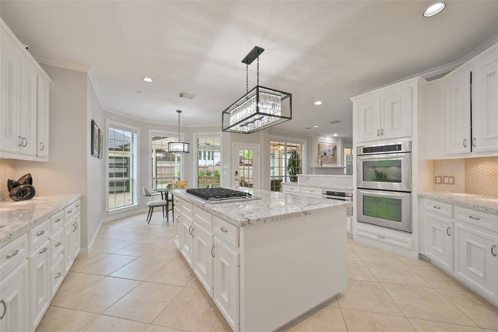 An alternate view of this bright and modern Chef's kitchen open to the breakfast area with large windows providing ample natural light and overlooking the beautifully landscaped backyard, pool and spa.