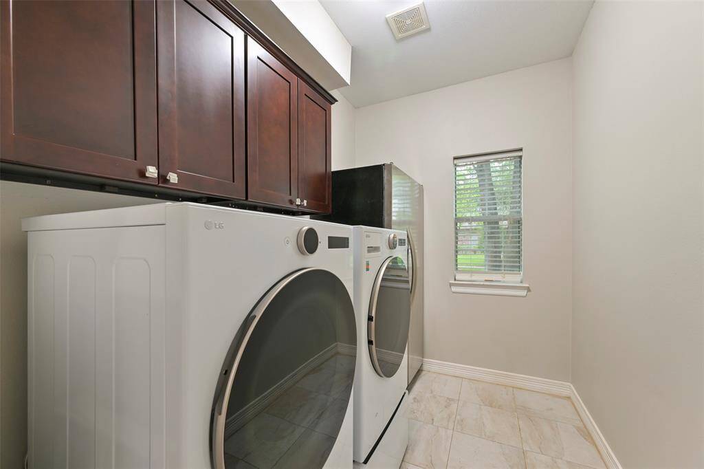 The spacious Laundry room with custom dark wood cabinets for added storage has room for additional refrigerator. A small window brings natural light into this area.