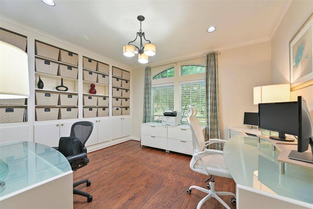 Bright and spacious home office/study featuring built-in shelving with ample storage. Large windows with elegant drapes provide plenty of natural light, complemented by stylish overhead lighting and hardwood floors. Ideal for productivity and organization.