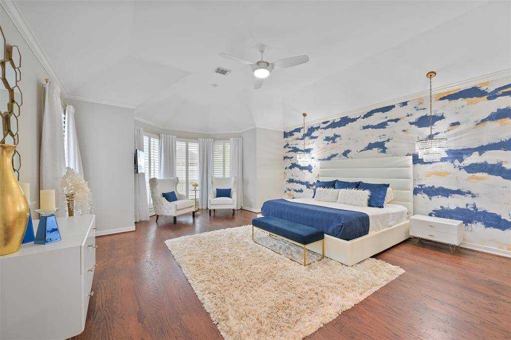 This spacious Primary suite with a contemporary design features hardwood floors, 2 custom chandeliers, and a stylish accent wall. The room features cozy seating area by bay windows with plantation shutters overlooking the landscaped backyard and offering ample natural light.