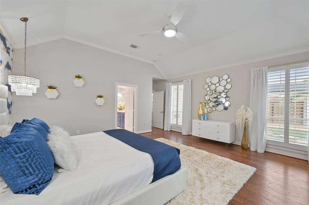 Another view of this spacious and bright Primary bedroom suite with high ceilings, modern accents inspired by Karen Nelson Designs, and large windows with plantation shutters. The room connects to the Primary bathroom ensuite, offering convenience and luxury.