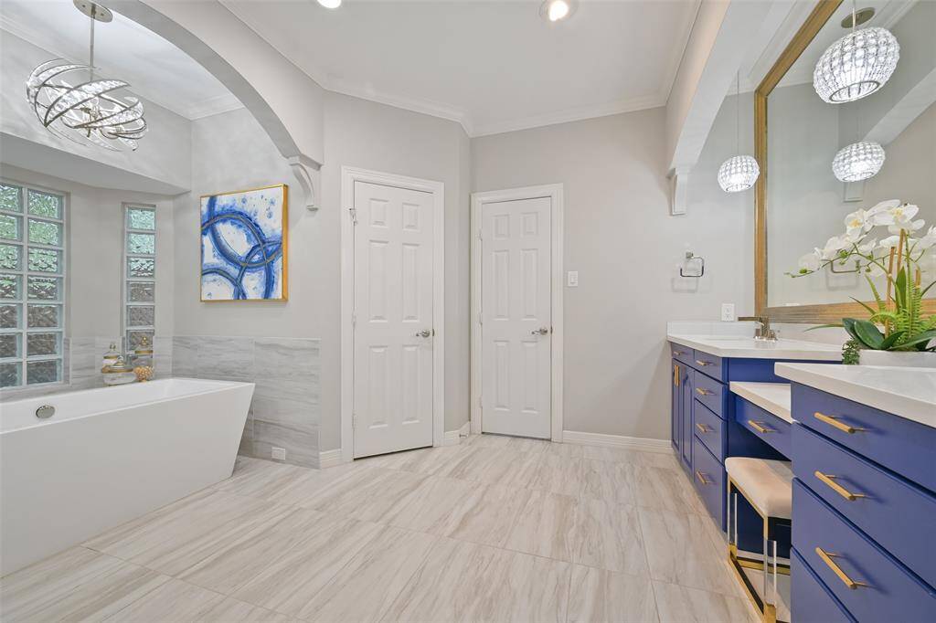 Another view of the luxurious Primary bathroom features elegant modern design with a freestanding soaking tub, large mirror, and stylish vanity. Natural light floods in through glass block windows, while contemporary light fixtures add a touch of luxury. Primary bathroom also features a large, custom-built walk-in closet.
