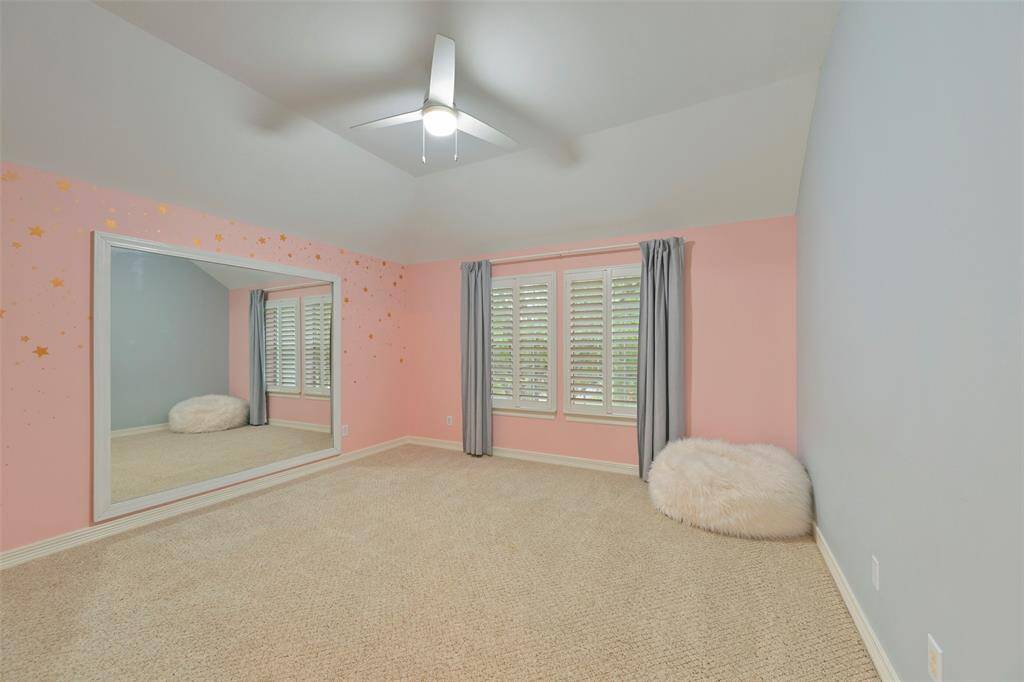 This cozy secondary Bedroom on the second floor features a large mirror, plush carpeting, large windows with plantation shutters overlooking the front, large walk-in closet, and a ceiling fan for added comfort. Ideal for a child's room or a creative space. This room was used as a dance studio.