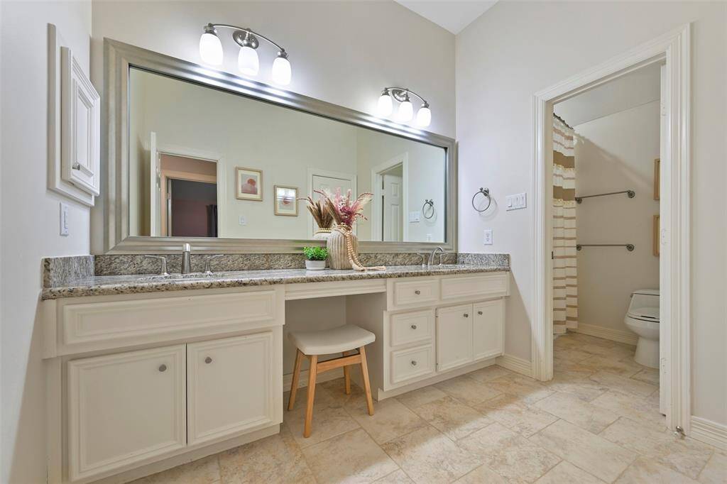This spacious bathroom features a double sinks with vanity, granite countertops, large mirror, ample storage, and a separate toilet area with a shower. The neutral tones and tile flooring create a clean, modern look. This bathroom is shared between the two bedrooms.