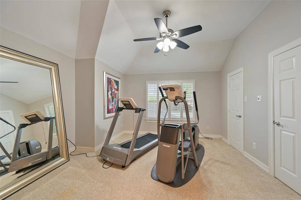 Another spacious Secondary bedroom on the second floor is set up as a home gym. It features a large walk-in closet, windows with plantation shutters, neutral walls, carpeted floor, and a ceiling fan, providing a bright and functional workout space.