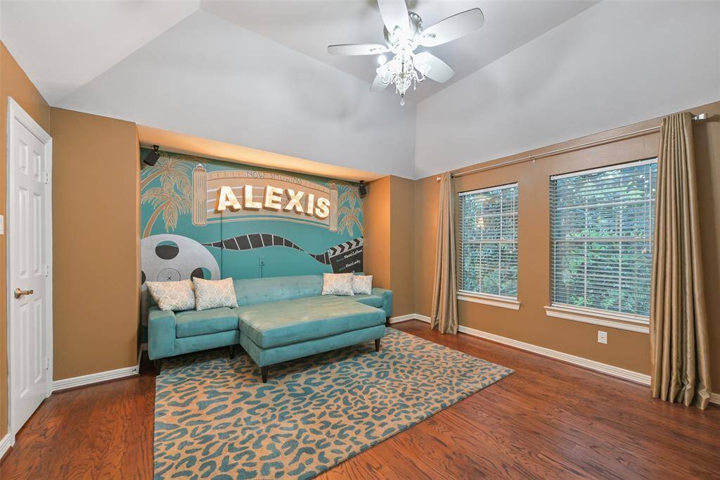 This spacious room features a stylish accent wall, large windows with elegant curtains offer natural light, complemented by a ceiling fan with a decorative light fixture. Perfect for a cozy lounge or media room, or simply another bedroom.