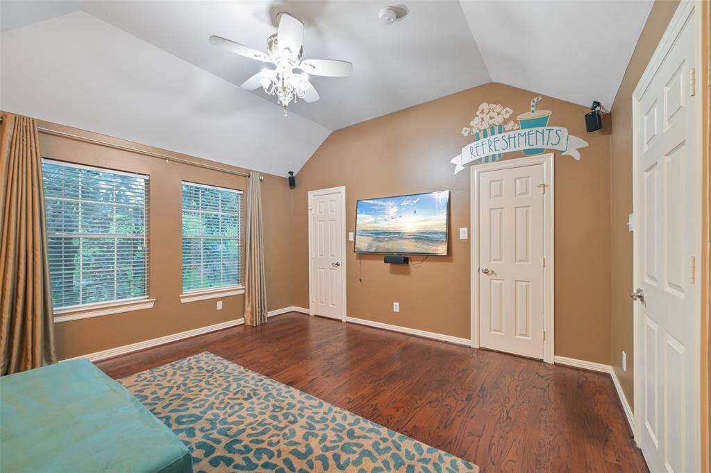 Another view of the media room with hardwood flooring, a vaulted ceiling, and walk-in closets.
