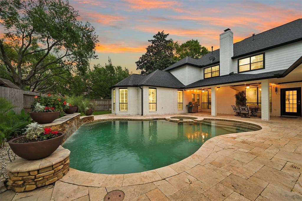Relax in this charming tropical backyard with a beautiful in-ground pool/spa surrounded by a spacious travertine patio. The outdoor area also offers a covered outdoor seating area, perfect for entertaining, and is set against a backdrop of lush greenery, offering a serene and private atmosphere.