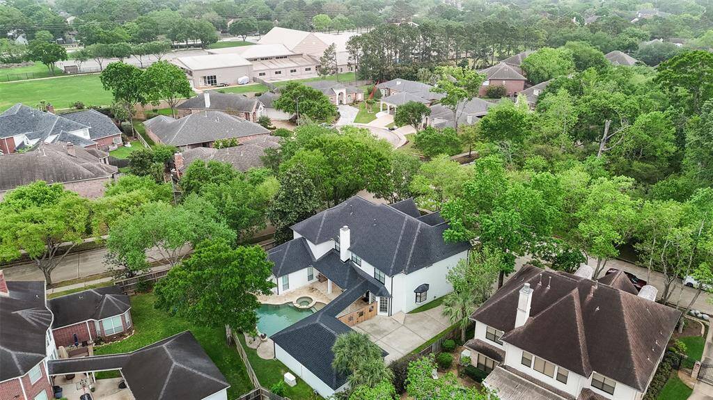 Aerial view of the home on the corner lot in a wooded setting across from the park.