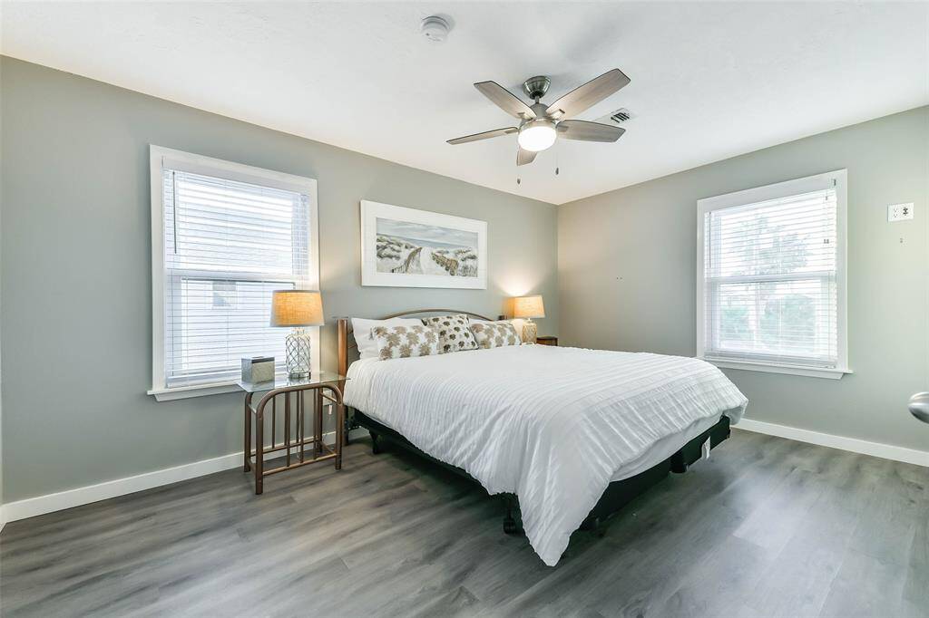 Spacious primary bedroom featuring a ceiling fan with an elegant light fixture, two-inch blinds, and two bright windows.
